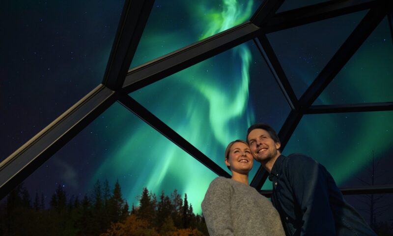 A couple inside a glass igloo under the norhern lights at Arctic SnowHotel & Glass Igloos.