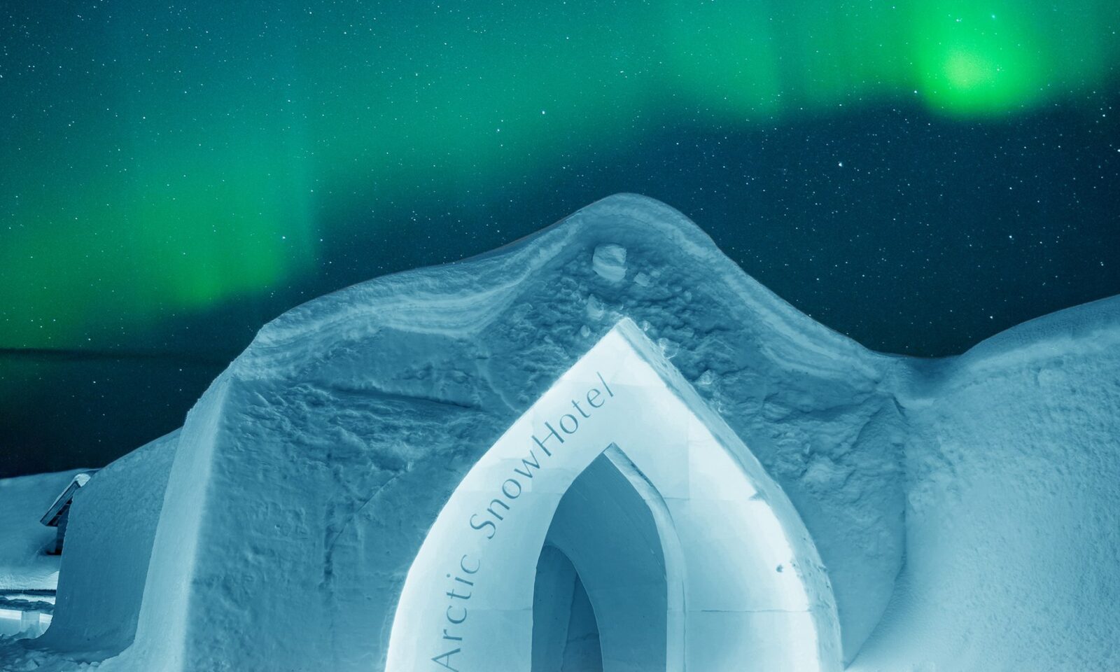 Arctic SnowHotelin sisäänkäynti ja taustalla revontulia.
